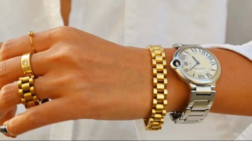 Hand wearing a silver watch and gold bracelets on a white background