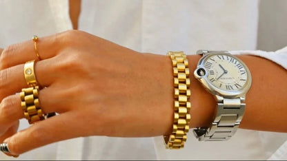 Hand wearing a silver watch and gold bracelets on a white background